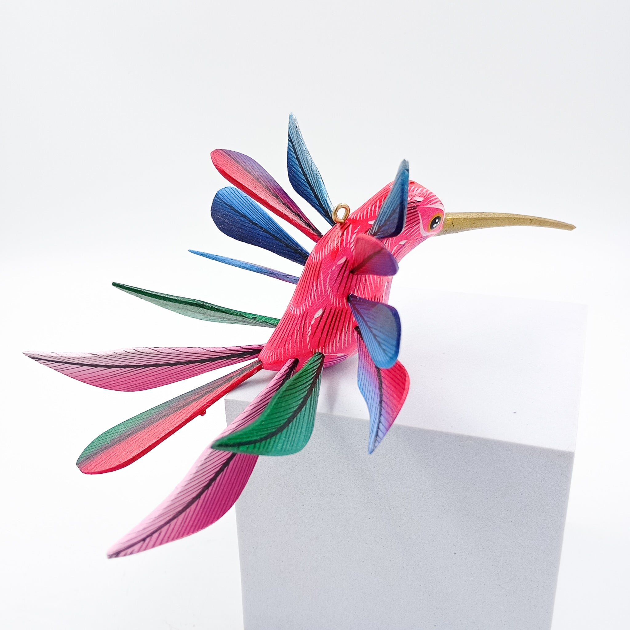 Colibrí rosa con alas de colores en madera de copal