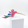 Colibrí rosa con alas de colores en madera de copal