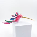 Colibrí rosa con alas de colores en madera de copal