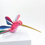Colibrí rosa con alas de colores en madera de copal